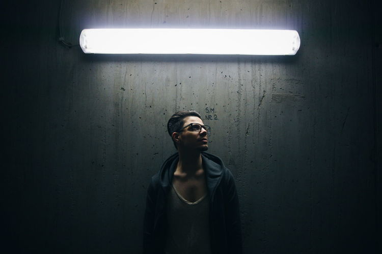 Man standing below fluorescent light against wall