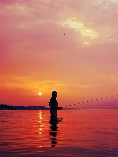 Silhouette man fishing in sea against sky during sunset