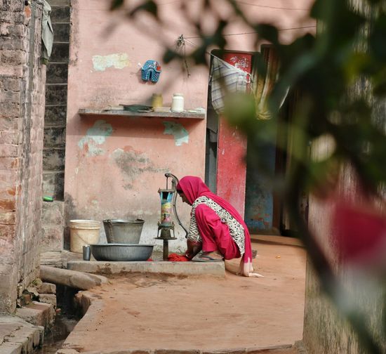 Woman washing laundry while sitting by hand pump