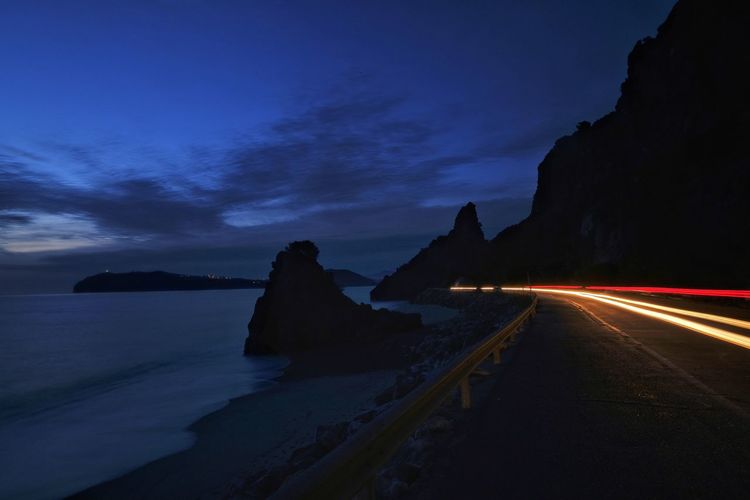 Light trails on road by sea at dusk