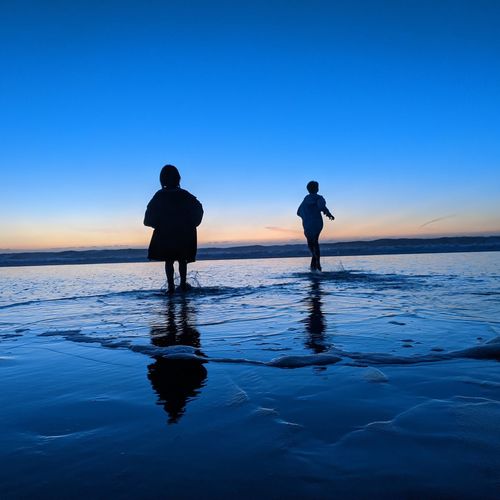 Silhouette children on beach against sky during sunset