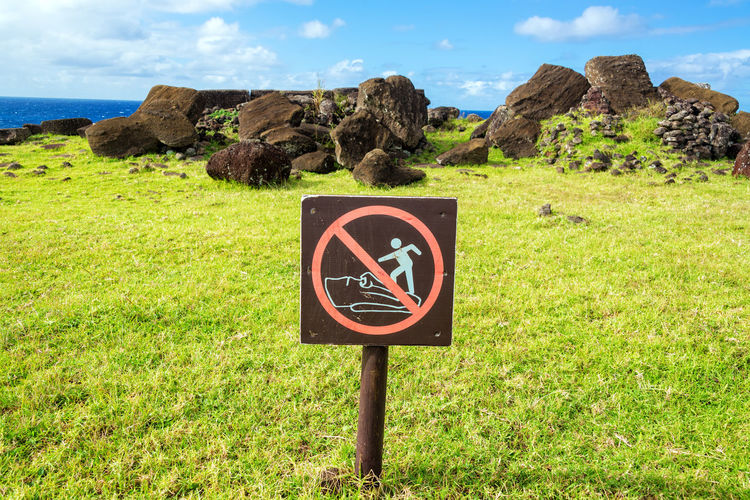 Warning signboard on grassy field against rocks at easter island