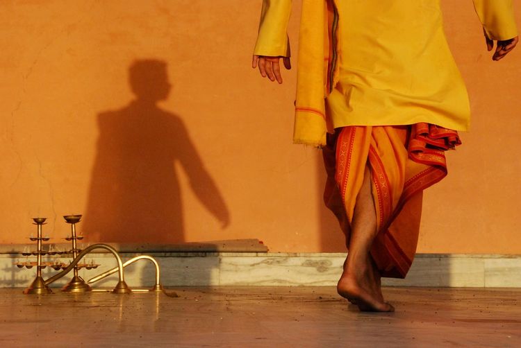 Low section of priest walking on floor against orange wall