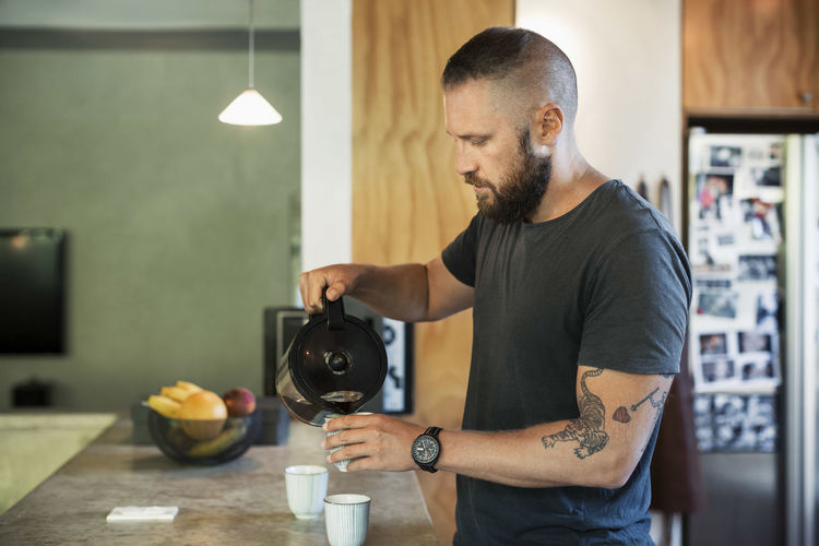 Man pouring coffee in cup in kitchen in home