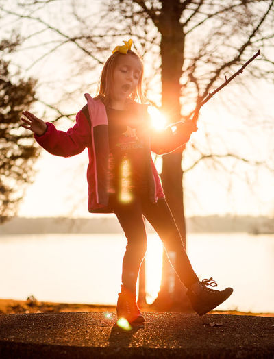 Young woman standing by tree against sunset sky