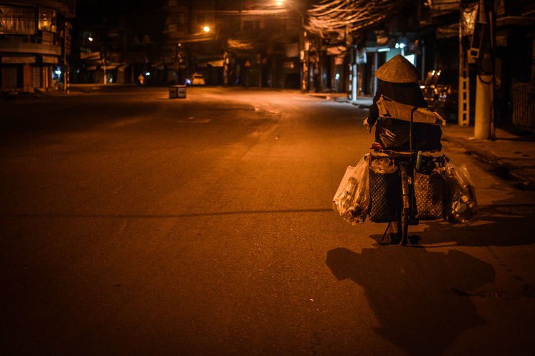 Rear view of waste picker riding bicycle on street at night in city