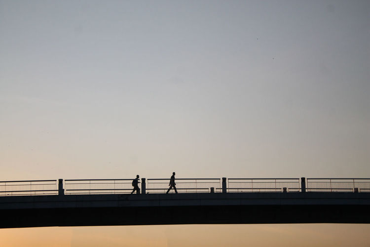Side view of silhouette people walking on bridge against clear sky