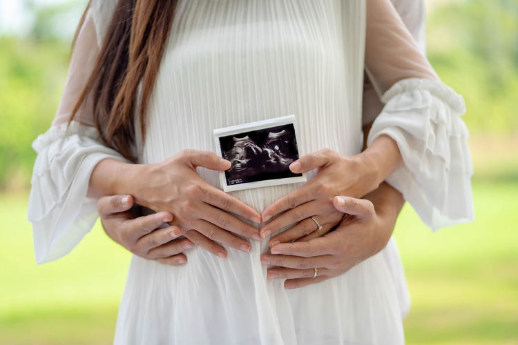 Midsection of pregnant woman holding ultrasound photograph standing outdoors