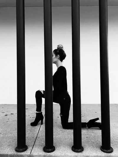 Young woman kneeling seen through prison bars