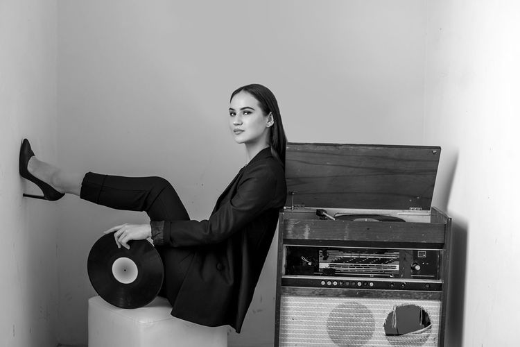 Portrait of woman sitting by vintage record player against wall