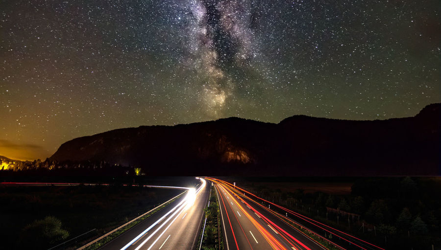 High angle view of light trails by mountains against star field