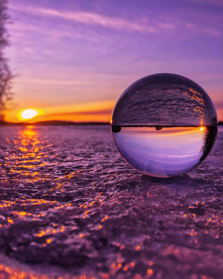 Close-up of crystal ball on water against sky during sunset