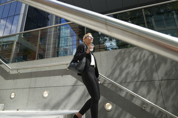 Mature woman with coffee cup walking on staircase against building exterior