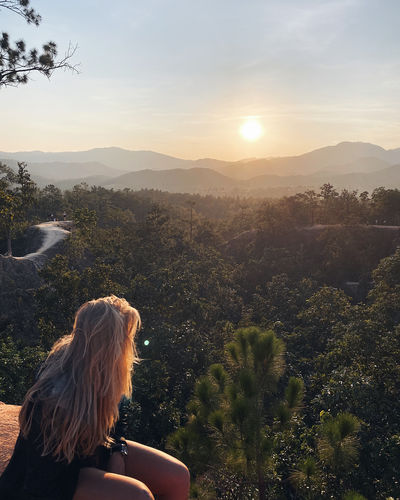 Woman looking at mountains against sky during sunset