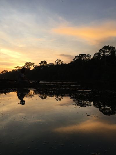 Silhouette trees by calm lake at sunset