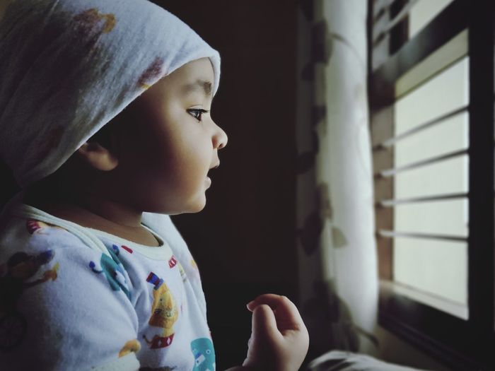 Close-up of cute baby girl looking through window