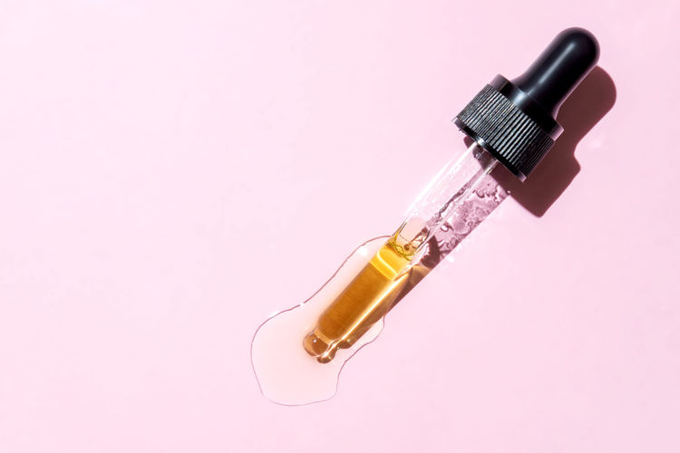 Retinol beauty face oil dripping from dropper with black lid on pink background. skin care cosmetic