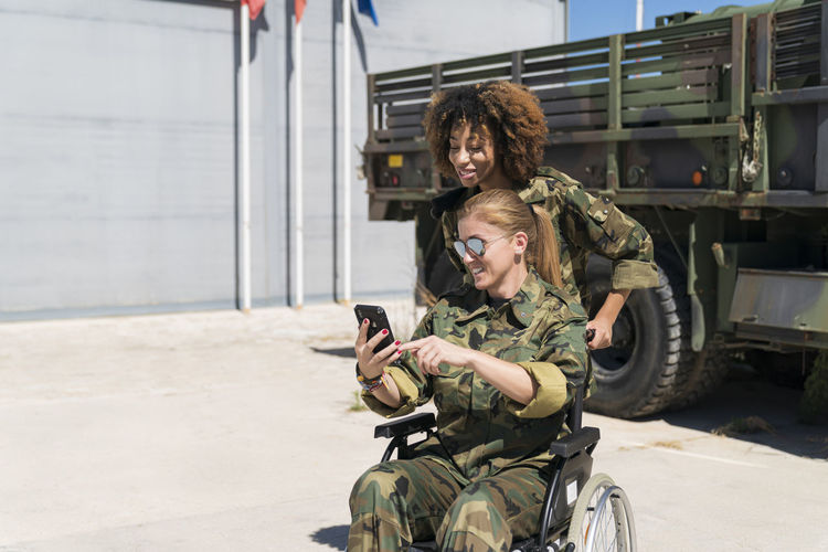 Smiling disabled female soldier taking selfie with young colleague against truck at army base on sunny day