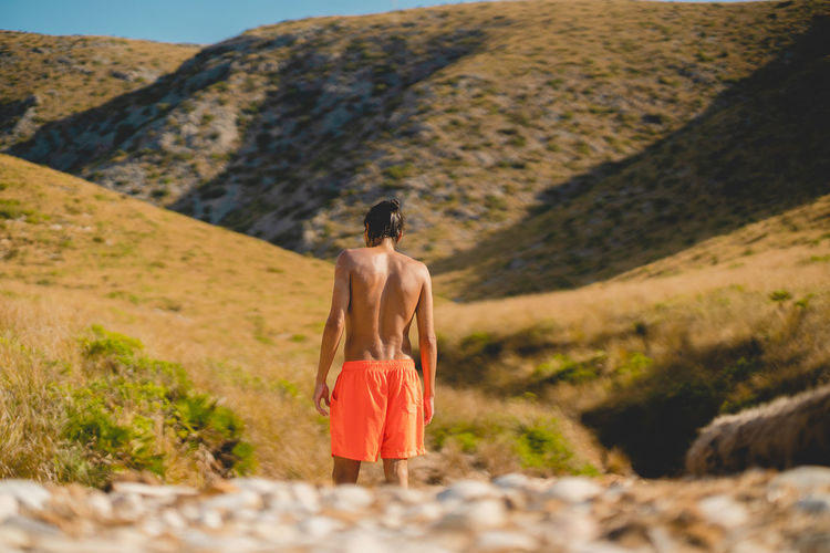 Rear view of shirtless man walking to mountain