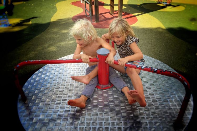 High angle view of happy siblings sitting on merry-go-round at park