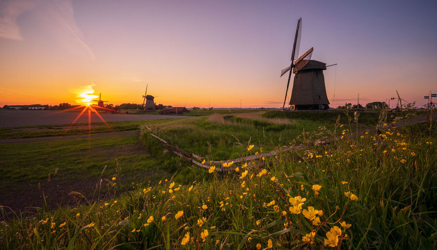 Traditional windmill on field against sky during sunset