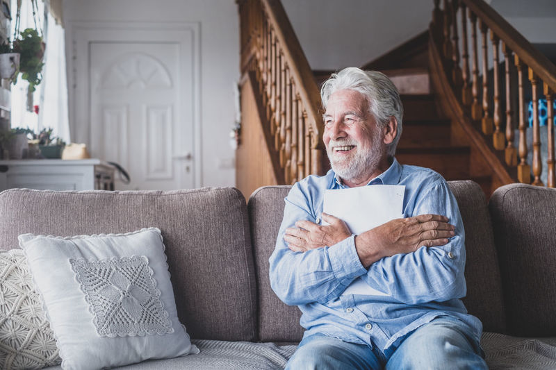 Senior man holding paper while sitting on sofa at home