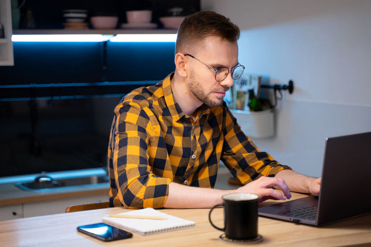 Portrait of male programmer in a yellow-black-gray shirt in glasses.coding at home. works on laptop.