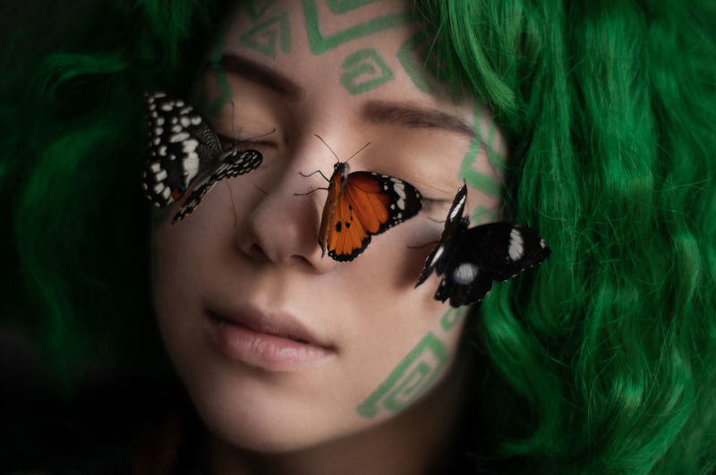 Close-up portrait of young woman with butterflies 
