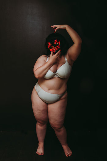 Young woman in lingerie holding mask standing against black background