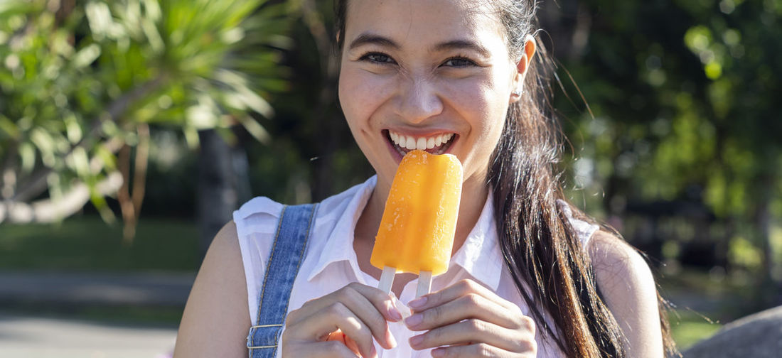Close-up portrait of cheerful young woman eating popsicle