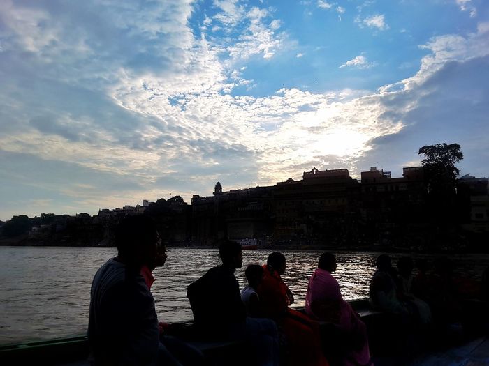 People sitting on riverbank against sky
