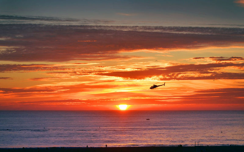 Rescue helicopter hovering over sea at sunset