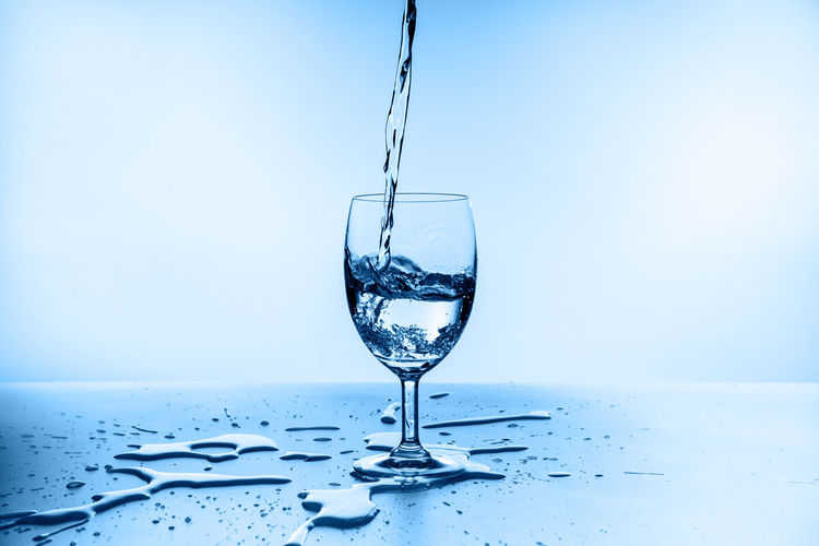 Close-up of glass pouring water against blue background
