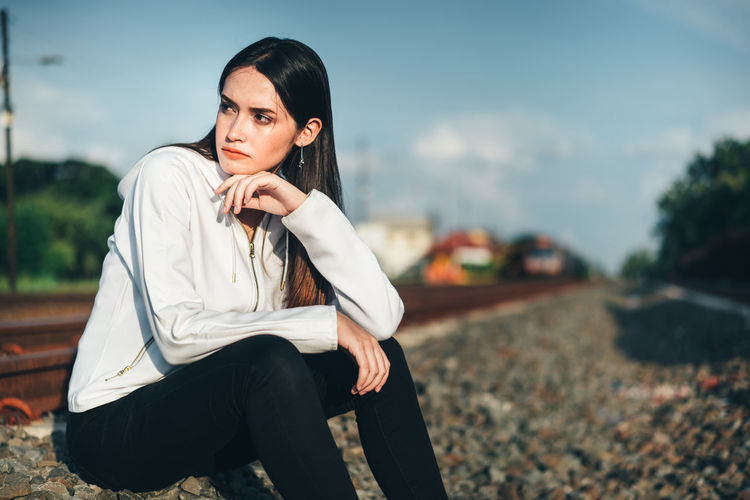 Thoughtful young woman sitting on railroad track