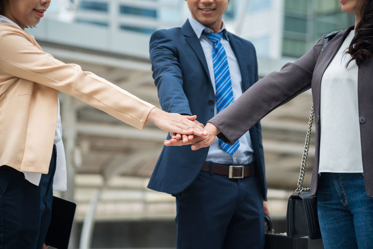 Midsection of business people huddling while standing against office building