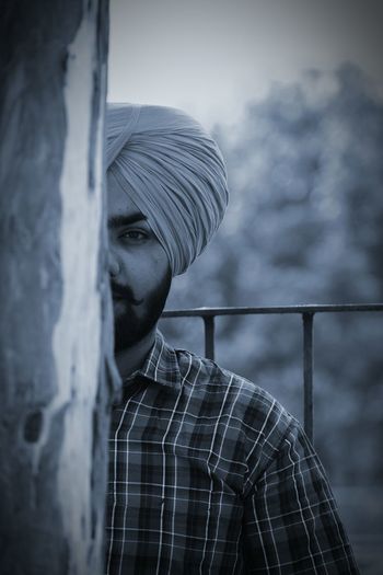 Cropped portrait of man wearing turban while standing behind wall