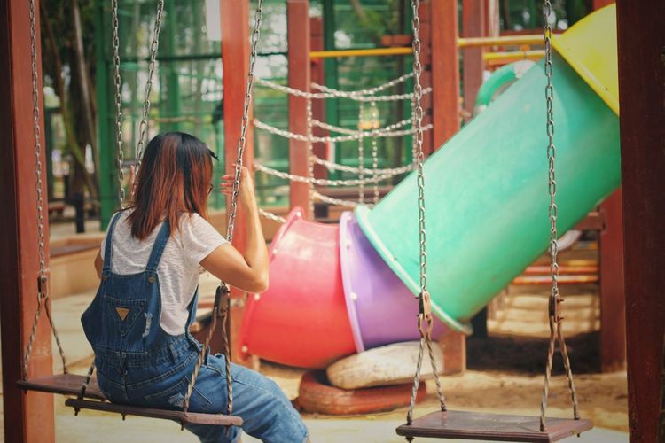 Rear view of woman sitting on swing in playground