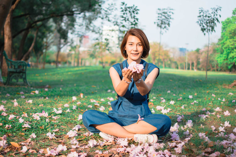 Portrait of woman holding flowers while sitting on field at park