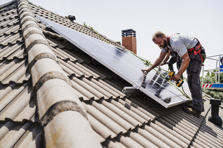 Electricians installing solar panels on rooftop of house