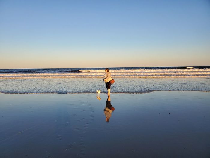 Woman with dog standing on beach against clear sky