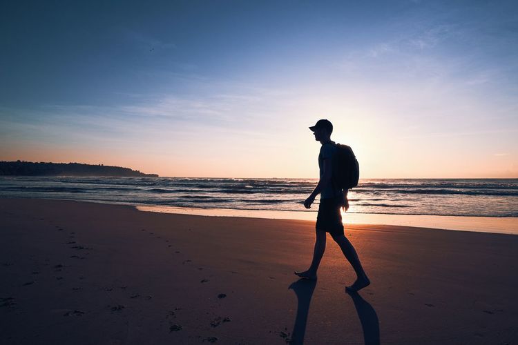 Silhouette man walking on beach against sky during sunset