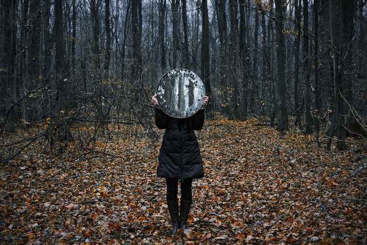 Low section of woman holding mirror while standing at forest during autumn