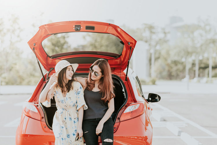 Smiling friends sitting on car trunk