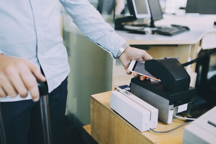 Midsection of businessman scanning ticket on smart phone at airport check-in counter