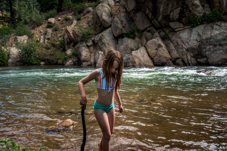 Young girl playing with a stick on the bank of a river