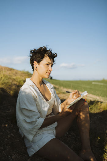 Woman with notebook contemplating while sitting on mountain