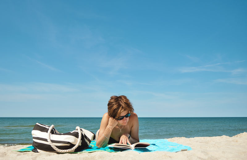 Middle aged woman reading a book on the beach at summer