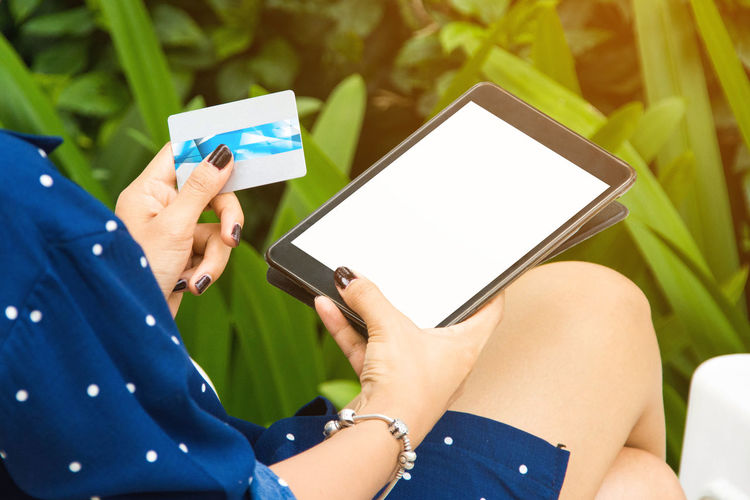 Cropped hands of woman holding credit card using digital tablet