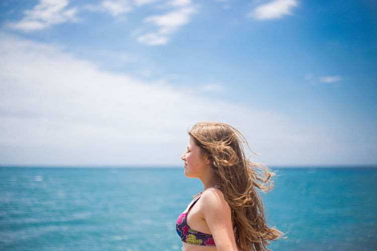 Side view of girl standing against sea and sky
