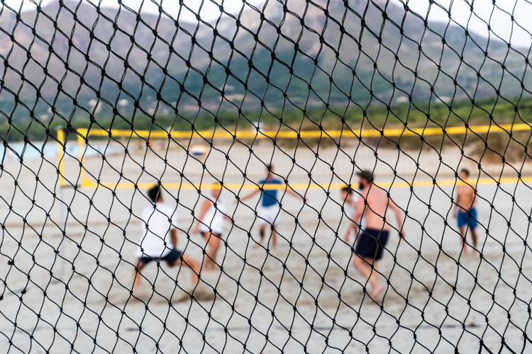 Friends playing beach volleyball seen through net